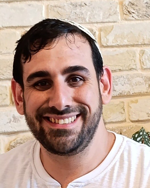 אריאל לוי מחייך, בחולצה לבנה מול קיר אבן בהירה